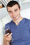handsome young man enjoying a glass of red wine sitting in a sofa at home
