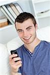 Charming young man sending a text smiling at the camera in the living-room
