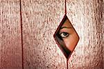Woman peeks through a diamond shaped hole in a wall. Horizontal shot.