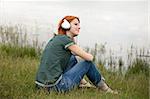 Young fashion girl with headphones sitting at lake coast.