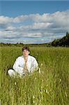 The young man meditates while sitting in a field