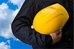 Yellow helmet at man hands on blue sky background