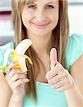 Smiling woman with thumb up holding a banana in the kitchen at home