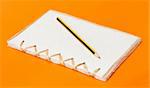 recycled notepad and pencil over an orange background