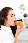 Charming hispanic businesswoman eating a doughnut in her office
