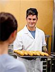 Glowing young male baker holding baguettes in the kitchen of his bakery