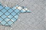 Broken glass fragments and chain link wired fence pattern against blue sky.