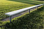 A brightly lit bench at a vacant soccer field.