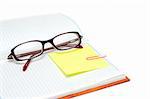 Spectacles on note pad with yellow bookmark and rose staple