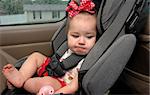 Infant sits in a car seat buckled up for safety.  She is making a funny face as this is not her favorite place to be.
