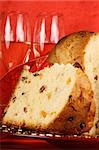Panettone the italian Christmas fruit cake served on a red glass plate over a red background with golden star decorations, ribbon and two glasses of spumante (sparkling wine). Selective focus.