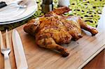 Whole barbeque chicken with cutlery and spices on wooden cutting board