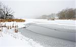 Winter day, snow-covered riverbank, ice, water and trees.