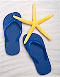 Summer Flip Flop Sandals with a Bright Yellow Starfish on a Sand Background.
