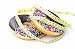 A chocolate frosted donut with colorful sprinkles with a yellow diet measuring tape wrapped around it isolated on a white background