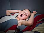 Young boy yawning, lieing in his bed