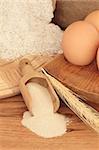 Baking ingredients of wholegrain flour on a wooden bread board, dried yeast in a scoop, eggs and wheat, against oak.