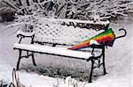 Colorful umbrella on the wooden bench in the park covered with snow.