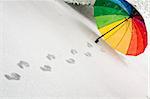 Colorful umbrella in the fresh fallen snow with some footprints around it.