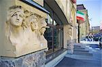 Entrance to cafe in city street with a group of people in background. The building was built before 1900, and the sculptures on the facade are public monuments and nobody can have copyright on them.