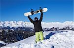 Snowboarder holding his snowboard over head