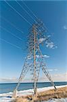 An electrical transmission tower carrying high voltage lines beside a lake in winter.