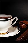 A white cup filled with hot luxury chocolate drink and chocolate bars on black background