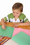 Young blond boy writing with crayons on colored paper