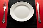 empty white plate on black table with knife and fork on red napkin by the sides of the plate