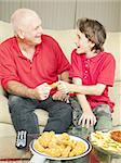 Father and son playfully fighting over a chicken wing as they watch the football game.