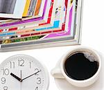 Pile of color magazines, coffee cup and clock isolated on white background