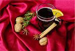 Hot spiced red wine with orange, cinnamon, star anise, walnuts and a branch of evergreen on red fabric (Selective Focus)