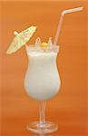 White Guanabana Smoothie in Cocktail Glass Decorated with a Paper Sunshade and a Physalis Fruit on Orange Background