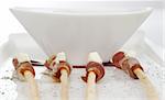 Thin ham slices wrapped around thin bread sticks and served on a long plate with a bowl in the background (Selective Focus)