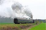 Steam retro train running through the countryside with lot of smoke over the sky