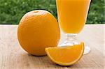 Orange and fresh orange juice in glass on green leaves background close-up