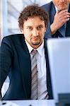 Young businessman working on laptop in the office with his colleague at the back.