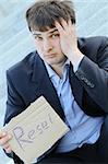 Young businessman sitting on the stairs of the building in hand bumga cardboard with the text "reset" with his other hand holding his head