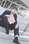 Young businessman sitting on the stairs of the building in hand bumga cardboard with the text "aaaa.." with his other hand holding his head