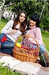 Mother and daughter sitting at a picnic on a blanket drinking wine next to a fruit basket