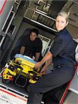 Two paramedics cheerfully removing empty gurney from ambulance