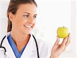 Close up of a smiling doctor with stethoscope looking at an apple in the surgery