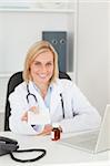 Smiling doctor holding prescription looks into camera in her office