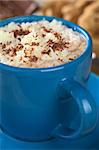 Hot chocolate with whipped cream and chocolate shavings in blue cup with cookies and chocolate in the back (Selective Focus, Focus on the top of the cream)