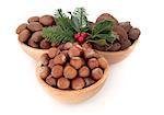 Hazelnuts, pecan and brazil nuts in wooden bowls with winter holly berry and pine fir leaf sprigs isolated over white background.