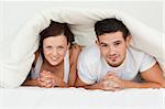 Happy couple hiding under their bvlanket in the bedroom