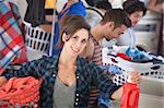 Beautiful Caucasian woman with clothes basket and detergent in the laundromat