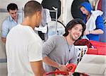 Man loads clothes in laundry machine with his friend