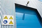 industrial unit with blue roller door and some warning signs