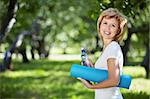 Mature woman in a park with a bottle and gym mat